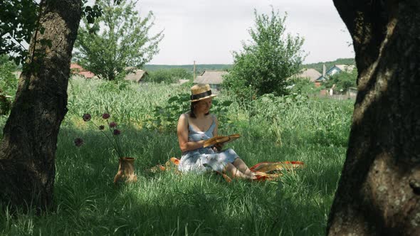 Attractive caucasian woman sitting on grass at green garden and reading book at summer sunny day.