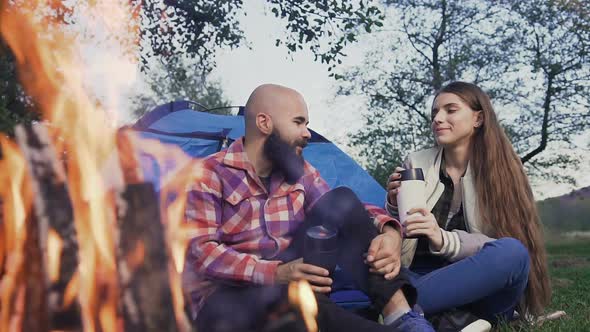 Happy Young Couple Sitting by the Fire in a Tent 