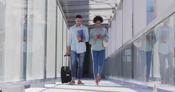 Video of diverse businessman and businesswoman walking with suitcase and talking