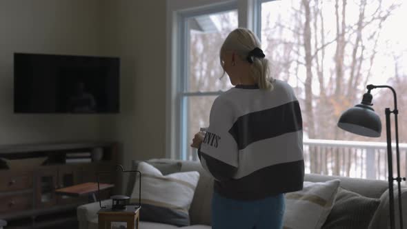 woman walking to the couch to lay down and scroll through tablet while drinking coffee in a nice hou