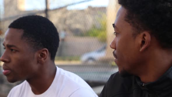 Two young basketball players talking on the sidelines of a street court.