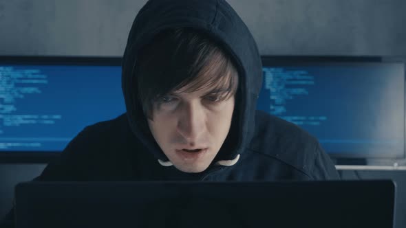 Man in Hood Sitting at Table and Coding on Laptop