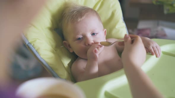 Mommy Feeds Cute Boy with Fresh Soup Puree in Highchair