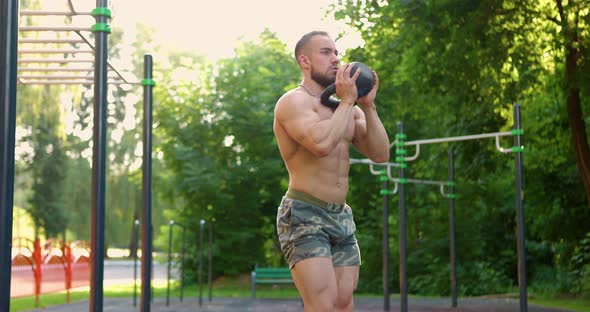 Athletic Man Squatting with Kettlebell Weight at the Park on Sports Ground