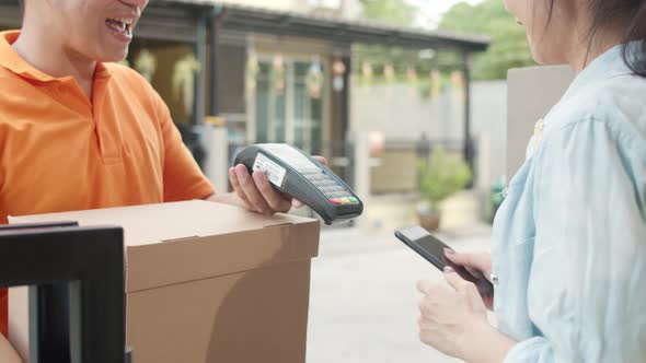 Asian women signing and pay via qr code on mobile phone for receive delivered parcels outdoors. .