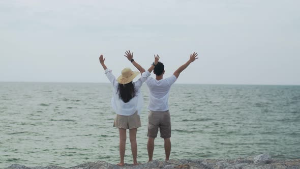 Asian couple in love celebrating success with raised arms into the air on the holiday weekend.