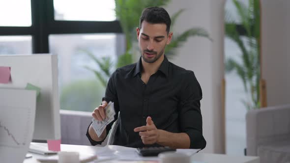 Young Rich Man Counting Cash Dollars Smiling Sitting in Home Office Indoors