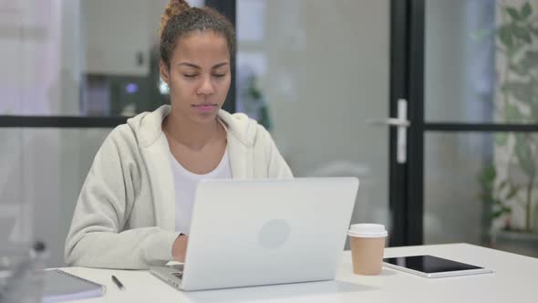 African Woman Pointing at Camera While Using Laptop in Office
