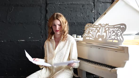 Emotional, angry woman in white  look at the notes.sitting near piano