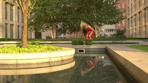 Beautiful Young Girl Dancing on the Street of a Modern City and Is Reflected in the Water