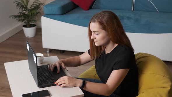 Young Woman Is Drinking a Cup of Coffee While Is Working at the Laptop From Home Office.