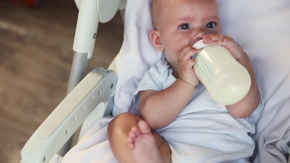 Cute Little Newborn Girl Drinking Milk From Bottle and Looking at Camera on White Background