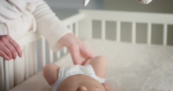 Caring Mother Stroking a Newborn Baby in a Diaper Lying on Her Back in Crib