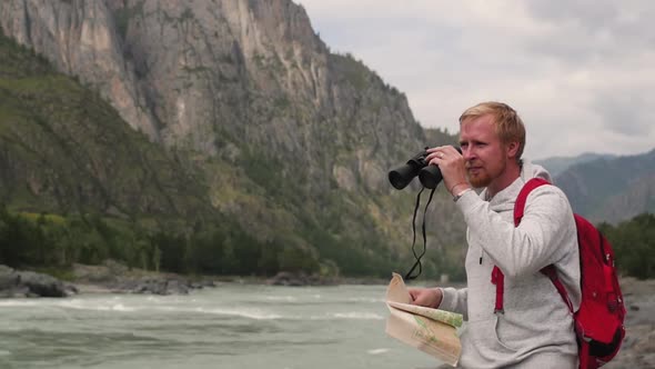 Man Travels in the Mountains. Tourist with Map and Binoculars Is Looking for the Way in the