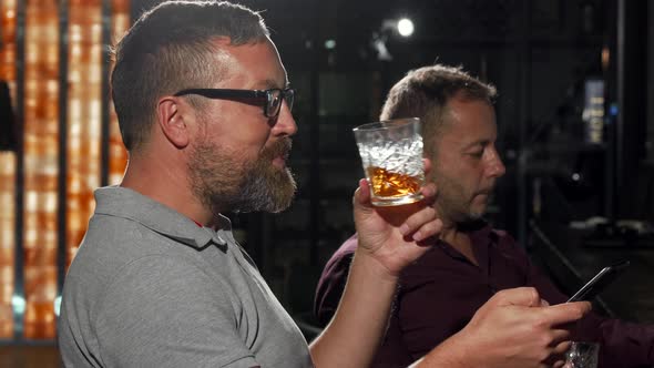 Happy Man Laughing While Drinking Whiskey and Messaging on His Smartphone