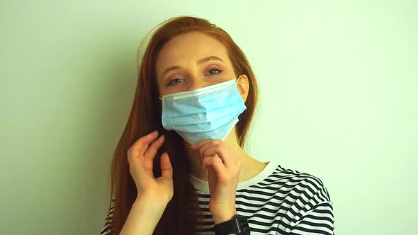 Young Woman Wears Protective White Medical Mask Puts on Medical Gloves and Glasses Preparing for