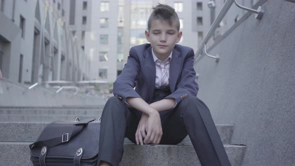 Pensive Well-dressed Cute Boy Sitting on the Stairs on the Street