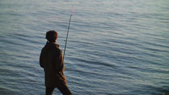 A Fisherman with a Fishing Rod Stands Against the Background of Blue Sea Waves