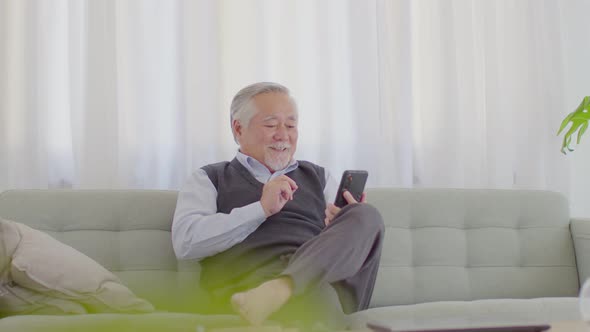 elderly asian man with white hairs sitting on sofa and using mobile phone Video Conference online