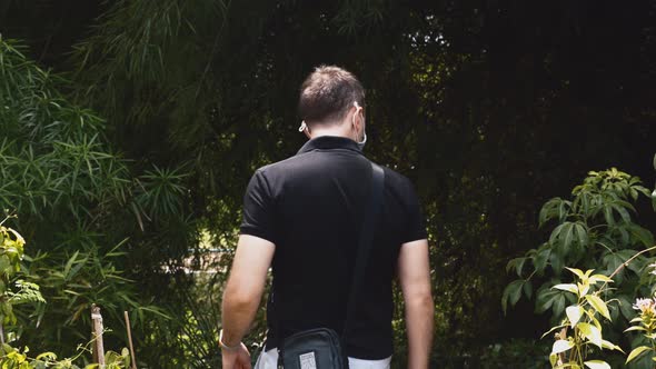 Back View of Man with Face Mask and Bag Walking Through Green Jungle