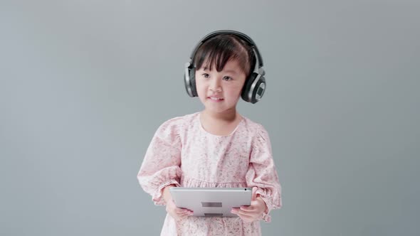 Girl with dress dancing and spinning with headphones in front of gray background.