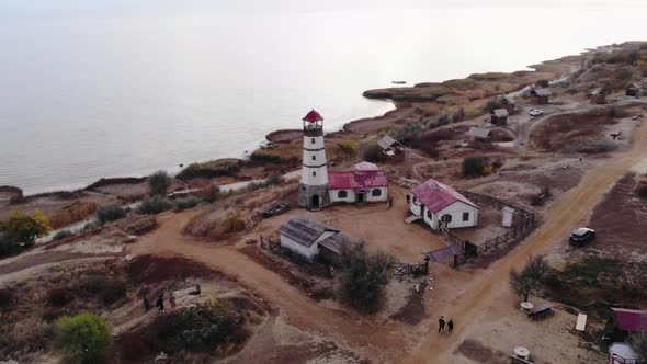 Shooting From a Drone of a Lighthouse at the Sea Against the Background of Hills and People Walking