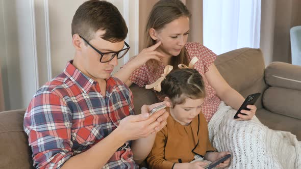 A Young Family Sits at Home with Mobile Phones and Surfs the Internet