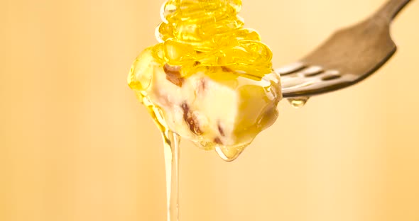 Liquid Organic Honey Dripping on a Fork with Cheese on a Light Background