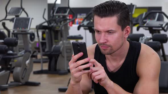 A Young Fit Man Works on a Smartphone in a Gym - Closeup