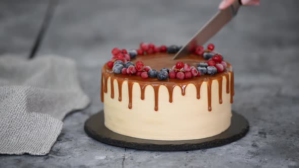 Female Hands Cutting Delicious Caramel Cake with Frozen Summer Berries