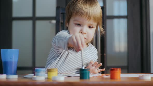 Toddler Dipping a Brush Into a Pot of Paint