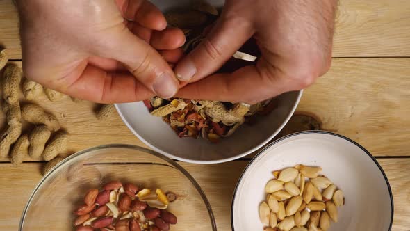 Slow motion footage of men's hands peeling peanuts into cups. Close-up