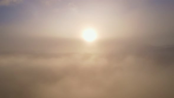 Drone view is raising above from the thick fog above the beautiful waves of fog at sunrise or sunset