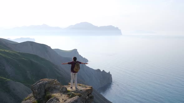 Young Woman Raises Her Hands Up Standing on the Top of a Mountain