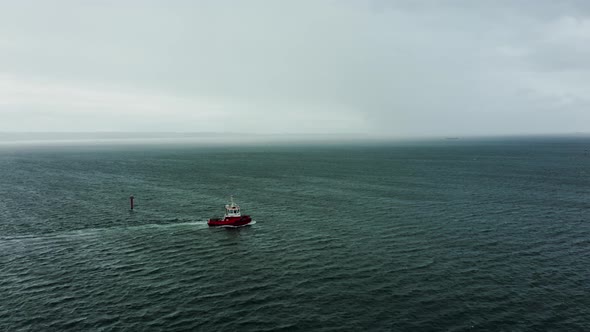 Drone Shot Tug Boat Goes to the Open Sea in Stormy Weather Behind a Cargo Ship