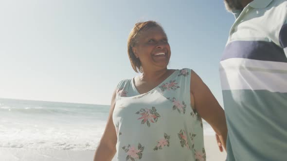 Smiling senior african american couple embracing and walking on sunny beach