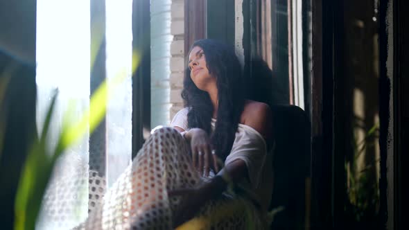 Romantic Brunette Lady is Relaxing on Windowsill and Viewing Garden in Summer Morning