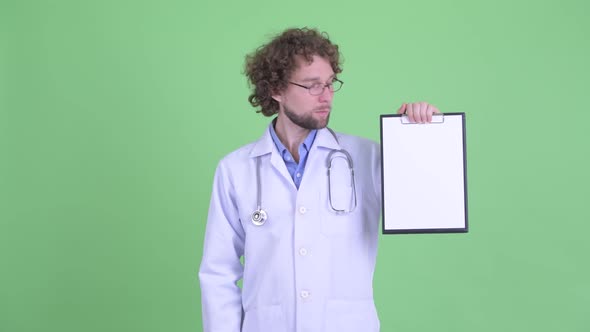 Happy Young Bearded Man Doctor Presenting with Clipboard and Giving Thumbs Up