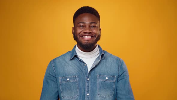 Surprised Young African Man Showing Thumbs Up Against Yellow Background in Studio