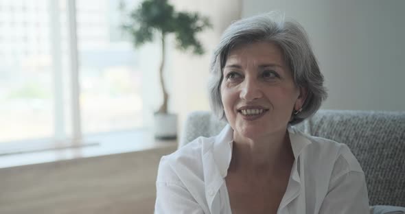 Happy Attractive Senior Adult Female Lady Staring at Camera Sitting Alone on Sofa at Home