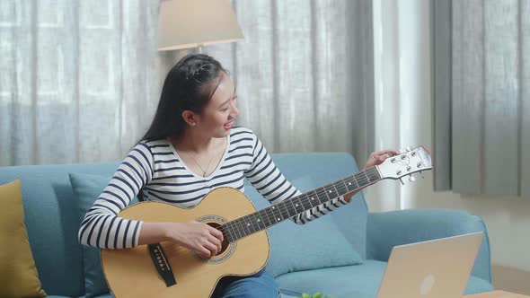Asian Woman Learning Pulling Strings Of Guitar By Laptop At Home