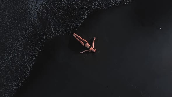 Drone View of Caucasian Woman in Black Bikini Lying on a Black Tropical Beach