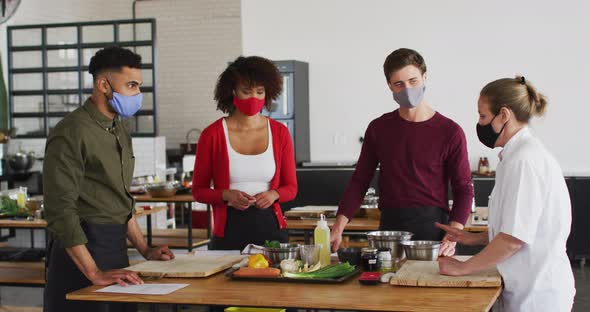 Caucasian female chef teaching diverse group wearing face masks