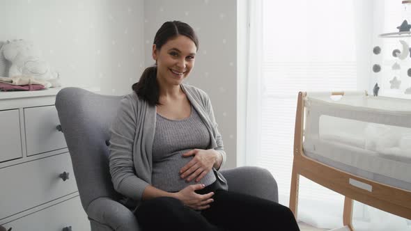 Portrait of woman in advanced pregnancy sitting in the armchair and stroking her abdomen. Shot with