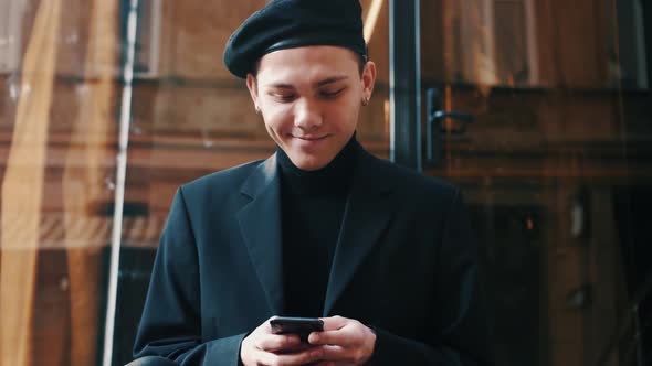 Handsome Smiling Startup Businessman in Beret Using Mobile Phone. Young Man Texting Messages