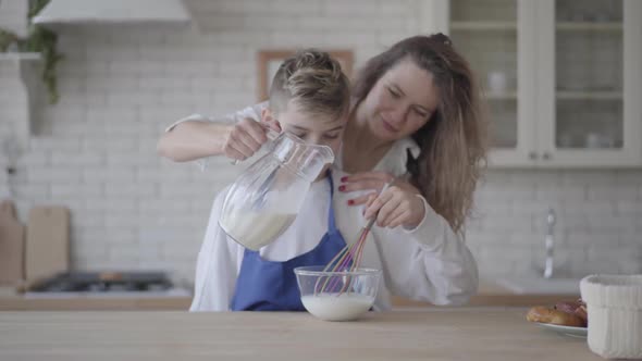 Portrait Cute Son Helps Mom in the Kitchen. The Boy Interferes with the Milk in a Glass Bowl Using