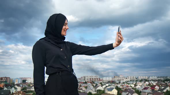 Happy Asian Woman in Black Hijab Posing Taking Selfie Smartphone Over Islamic City and Dramatic Sky
