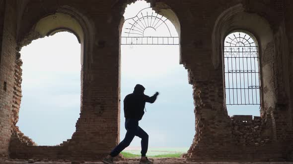 Man boxer in the hood trains beats in an abandoned building. Shadow Boxing on a beautiful background