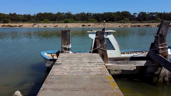 An old wooden pier with a vintage and grungy fishing boat tied to it - low altitude flyover or push