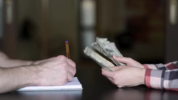 Counting money at home. Female hands count dollars, and a man makes notes